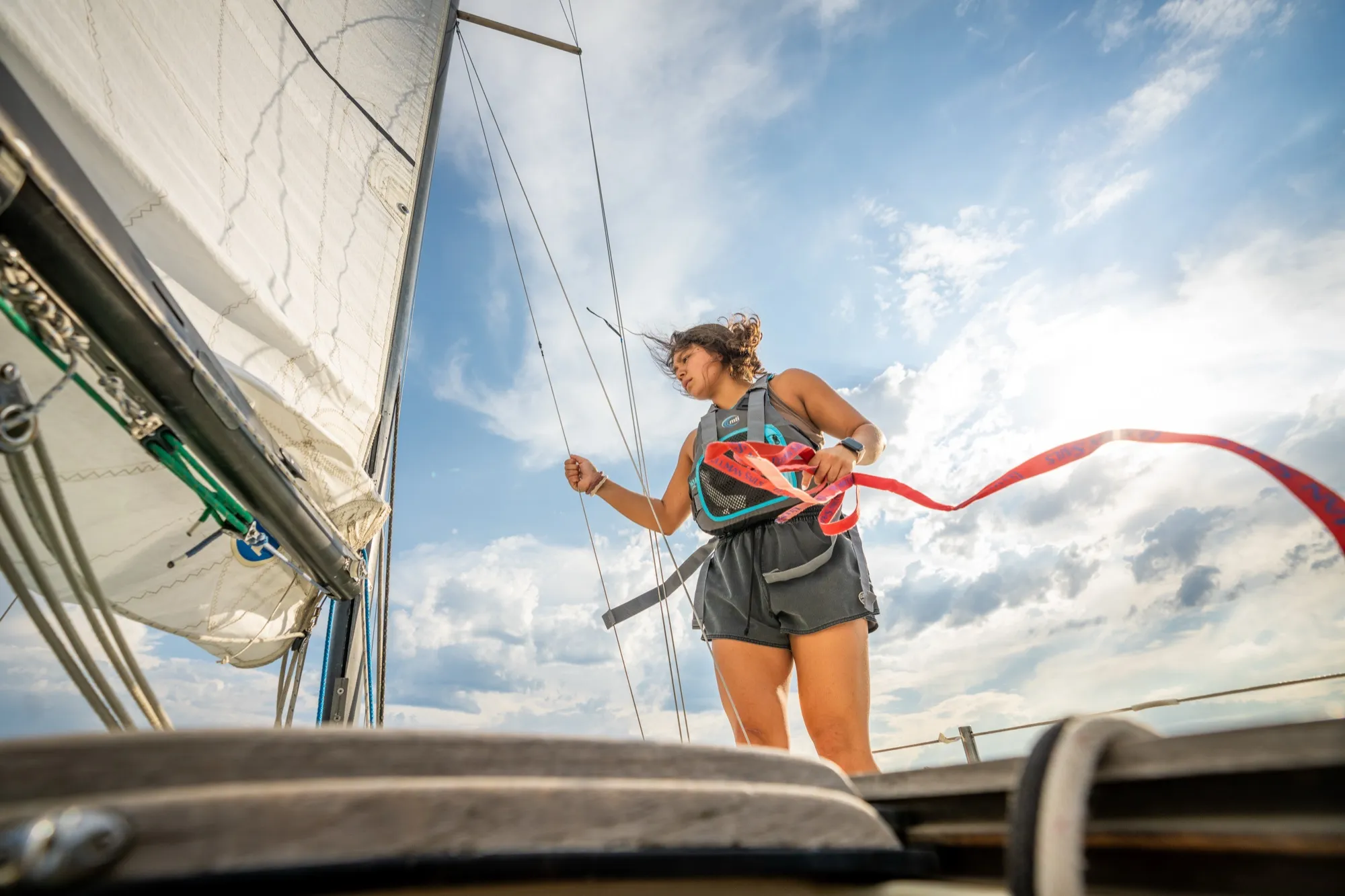 A woman trimming the sail on a sailboat under an open sky